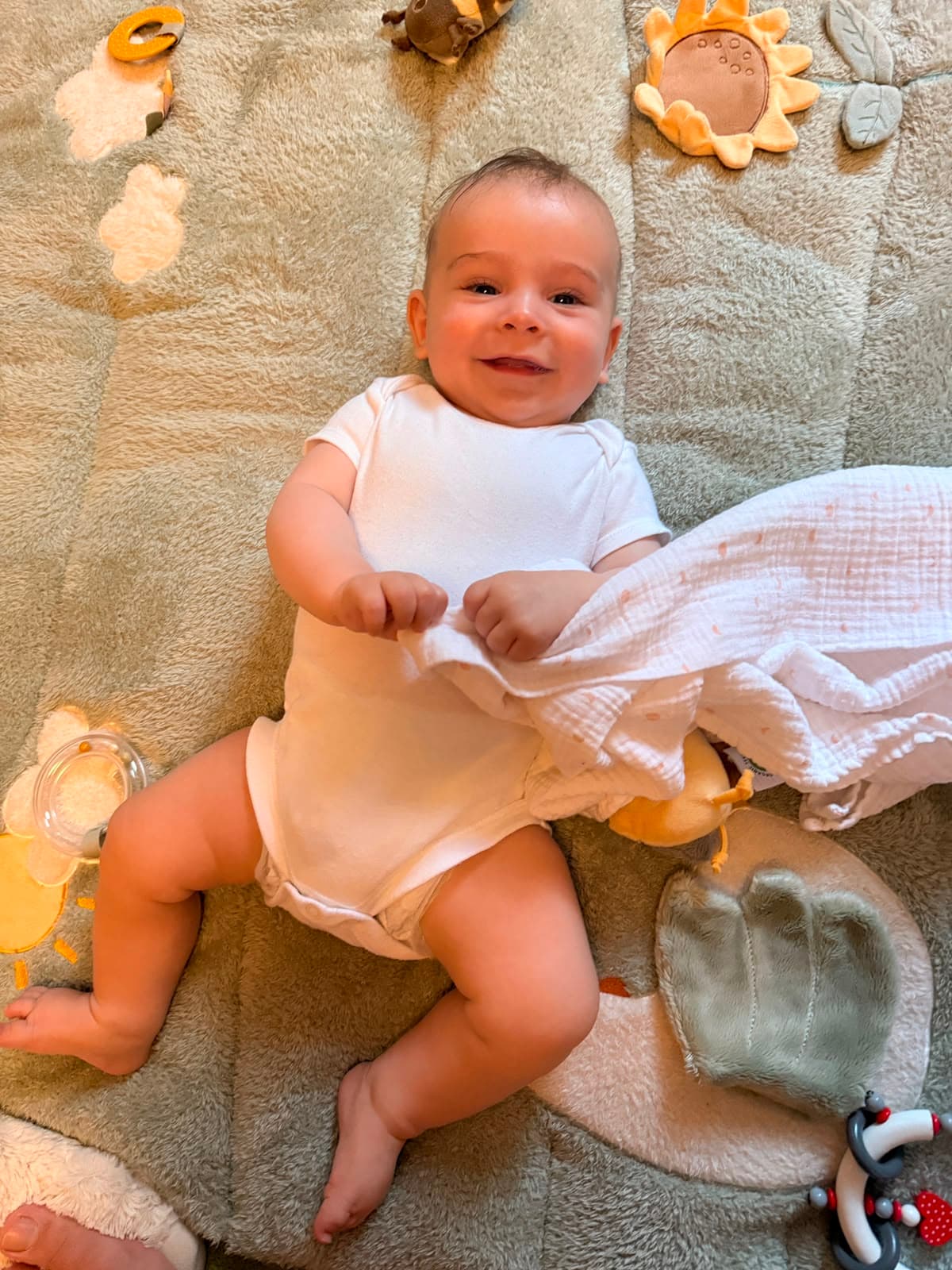 Ausgangsbild: Schnappschuss eines lachenden Babys auf einer Spieldecke mit Spielzeug ringsum