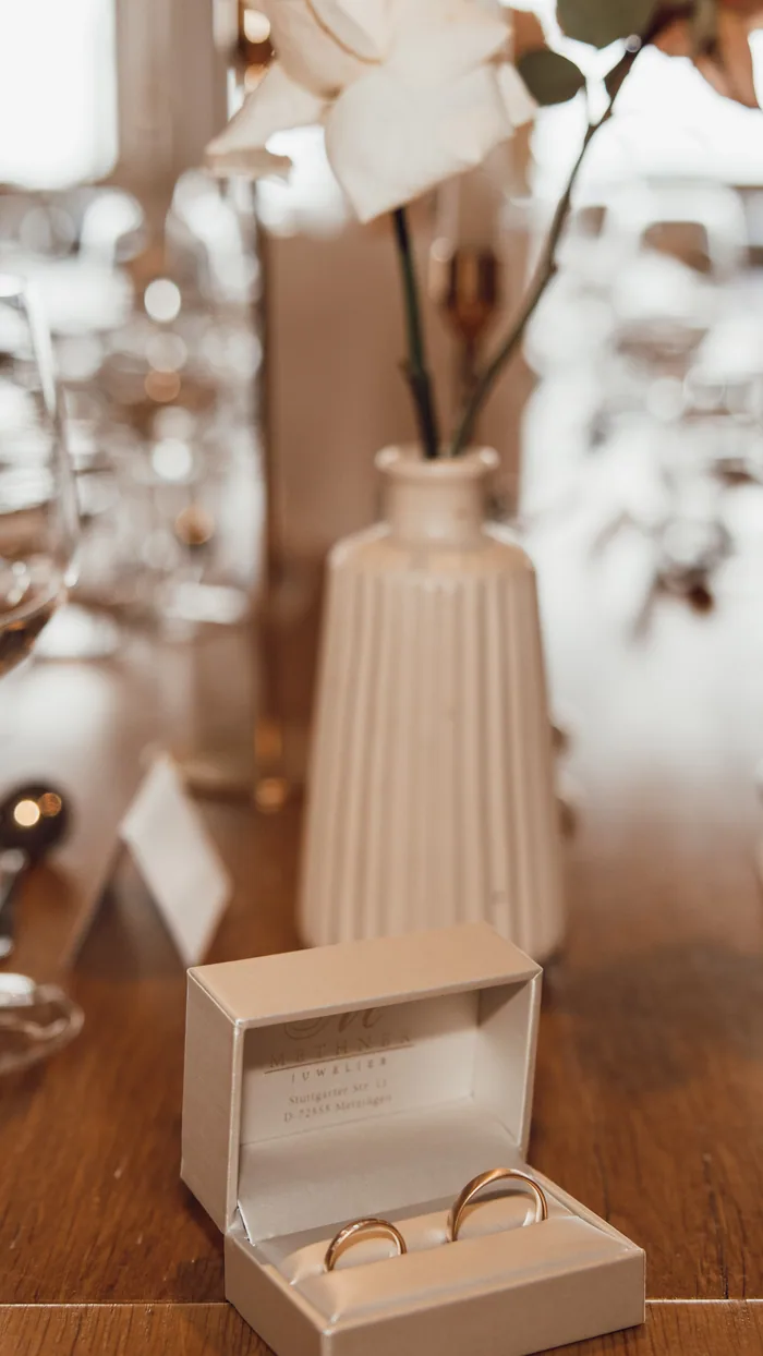 Derselbe Moment als Hochformat: Rose, Vase und Ringschatulle stehen übereinander auf einer Achse